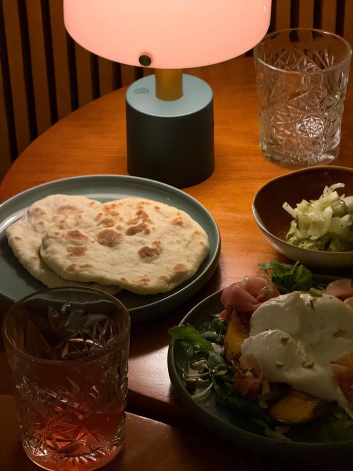Pão achatado, dip de grão-de-bico verde e pêssego grelhado com burrata numa mesa do DOM.